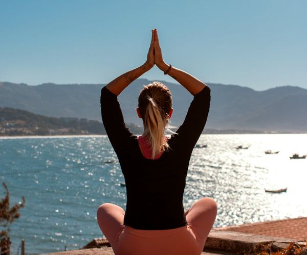 A person sitting in a meditative lotus pose outdoors at sunrise.